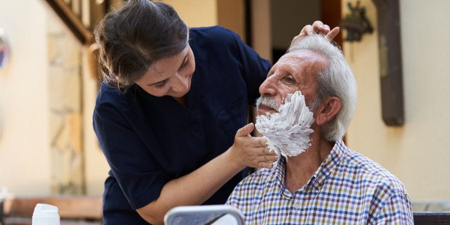 caregiver shaving elderly man