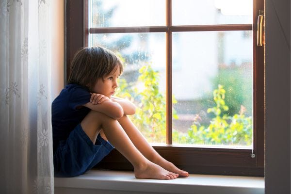 Child sitting on a window sill, looking upset.