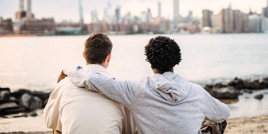Person hugging another person, looking at a city skyline in the distance.